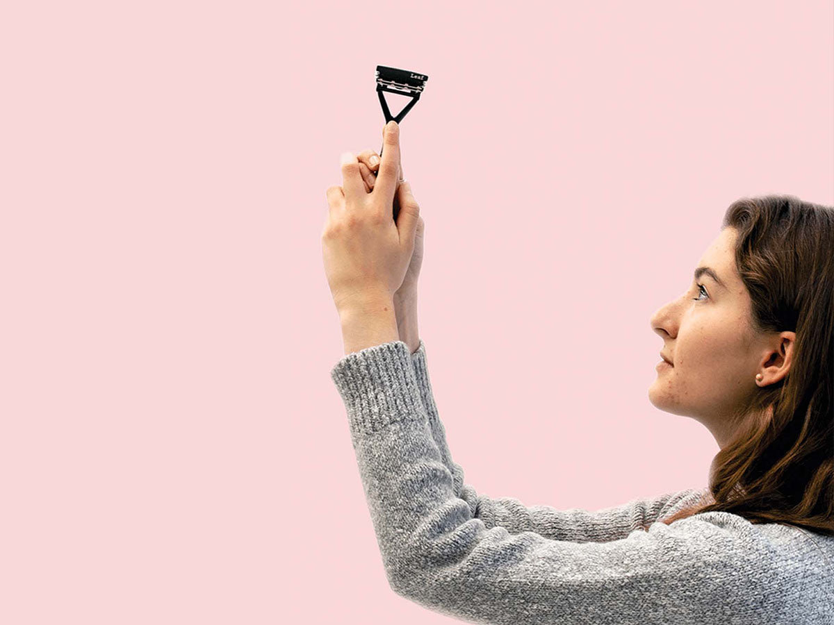 Person in profile, holding up a Leaf Razor and looking at it on a pink background