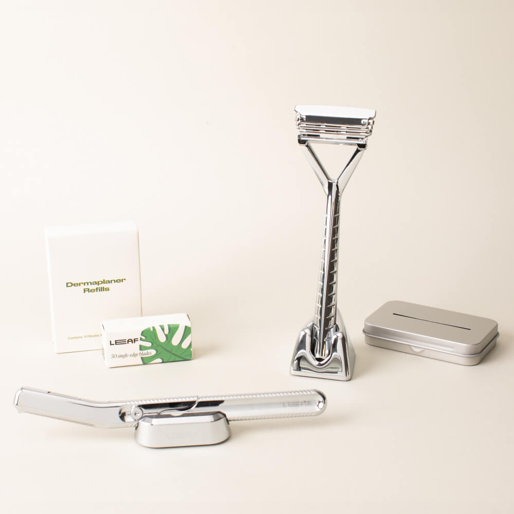 The chrome full face and body kit displayed with the leaf razor, dermaplaner, a stand and blades, for each, and the recycling tin