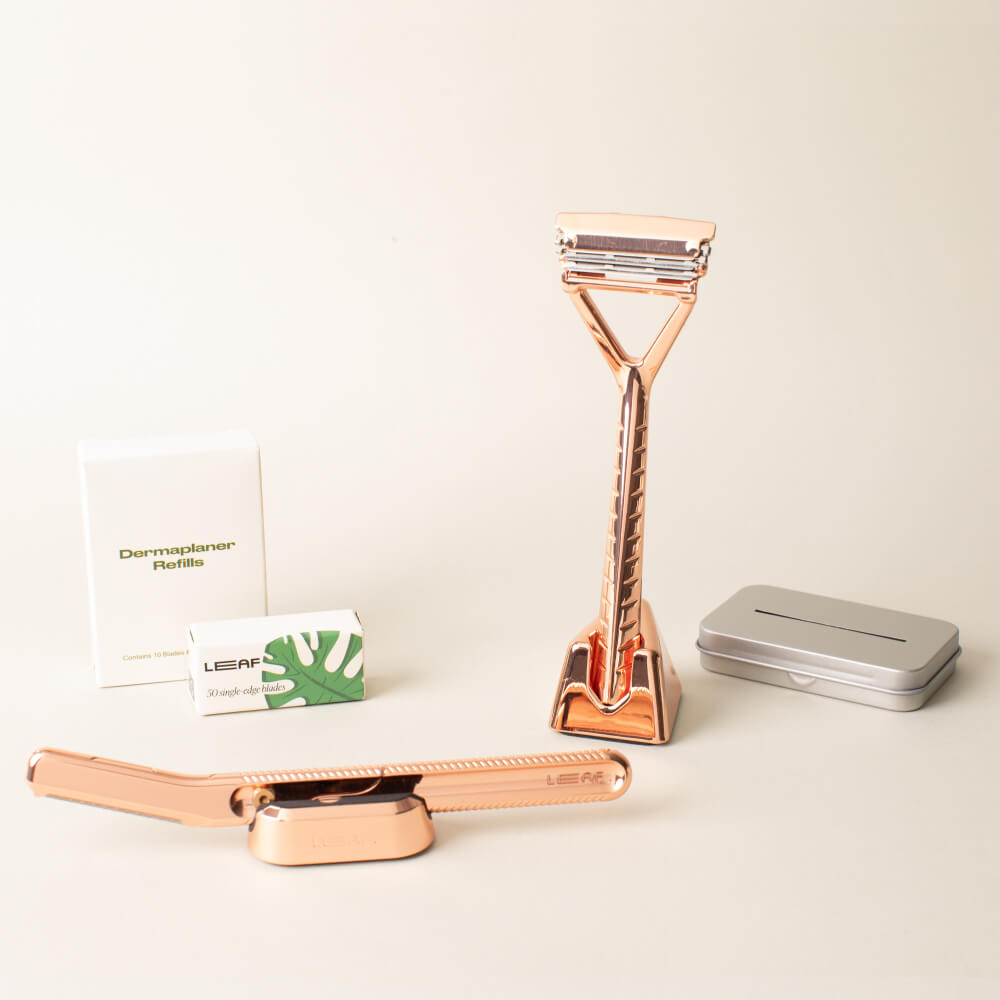 The rose gold full face and body kit displayed with the leaf razor, dermaplaner, a stand and blades, for each, and the recycling tin