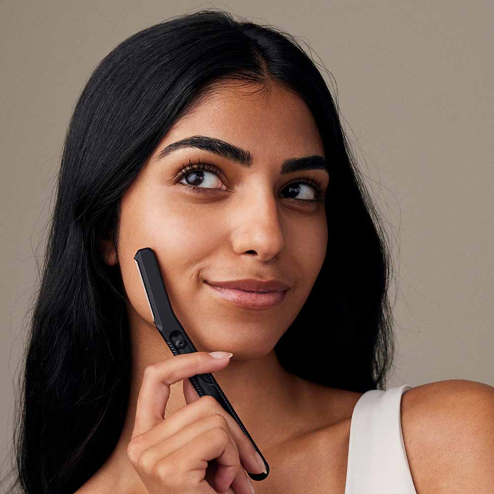 Woman holds dermaplaner near her cheek